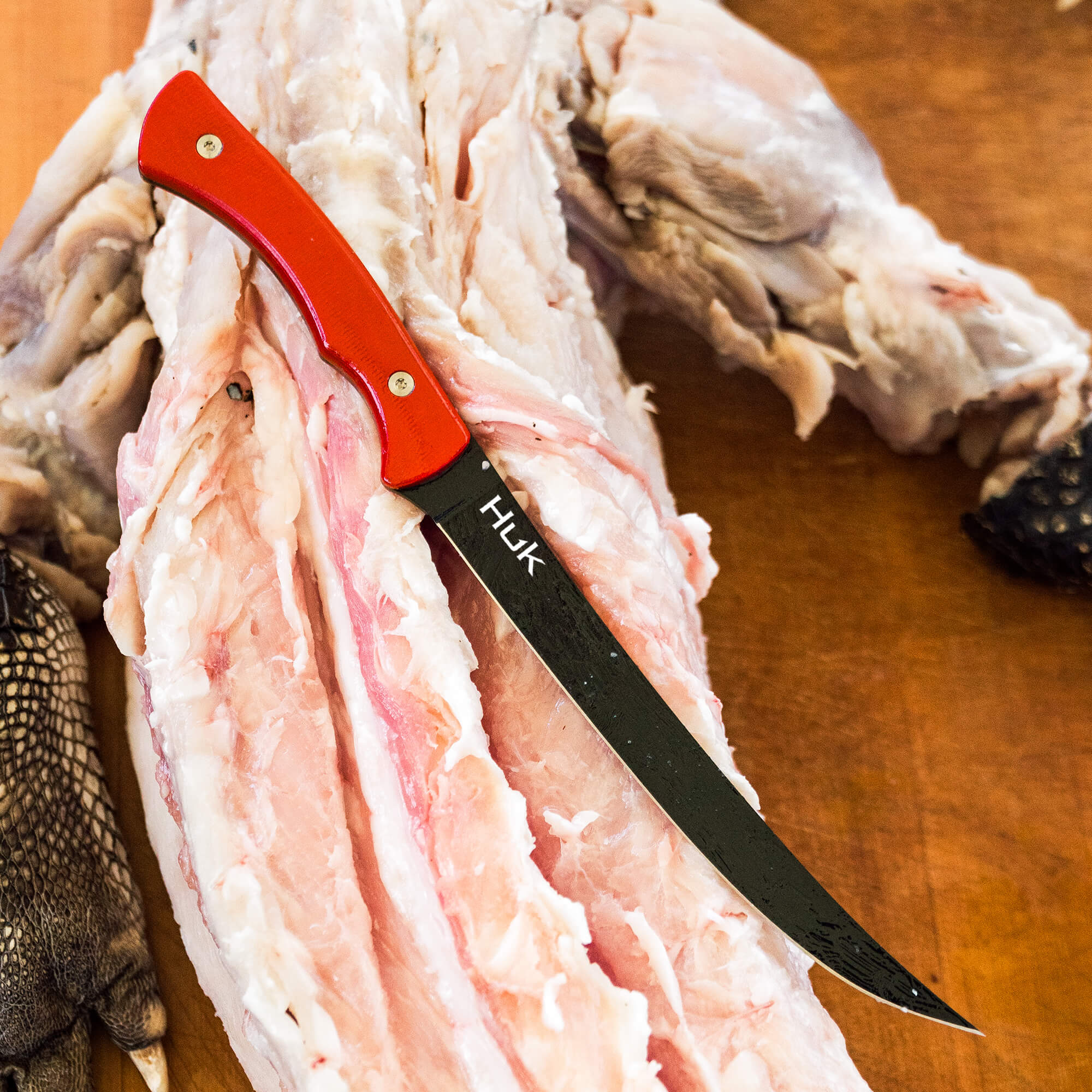 HUK Flathead Fillet knife resting on a fish carcass, showcasing its curved blade and red handle for precision filleting.