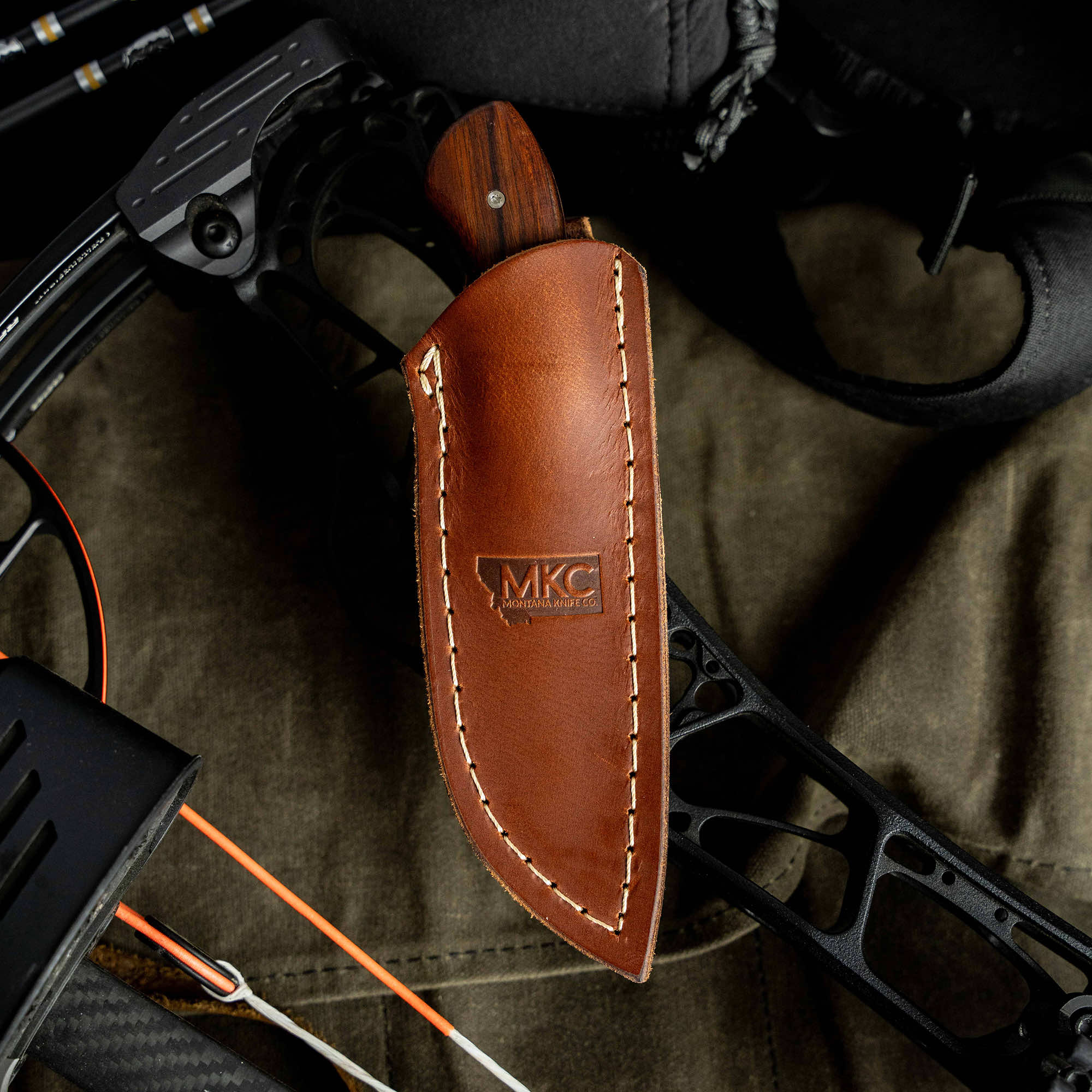 MKC Elk Knife in a leather sheath resting on a bow, showcasing craftsmanship for outdoor enthusiasts.