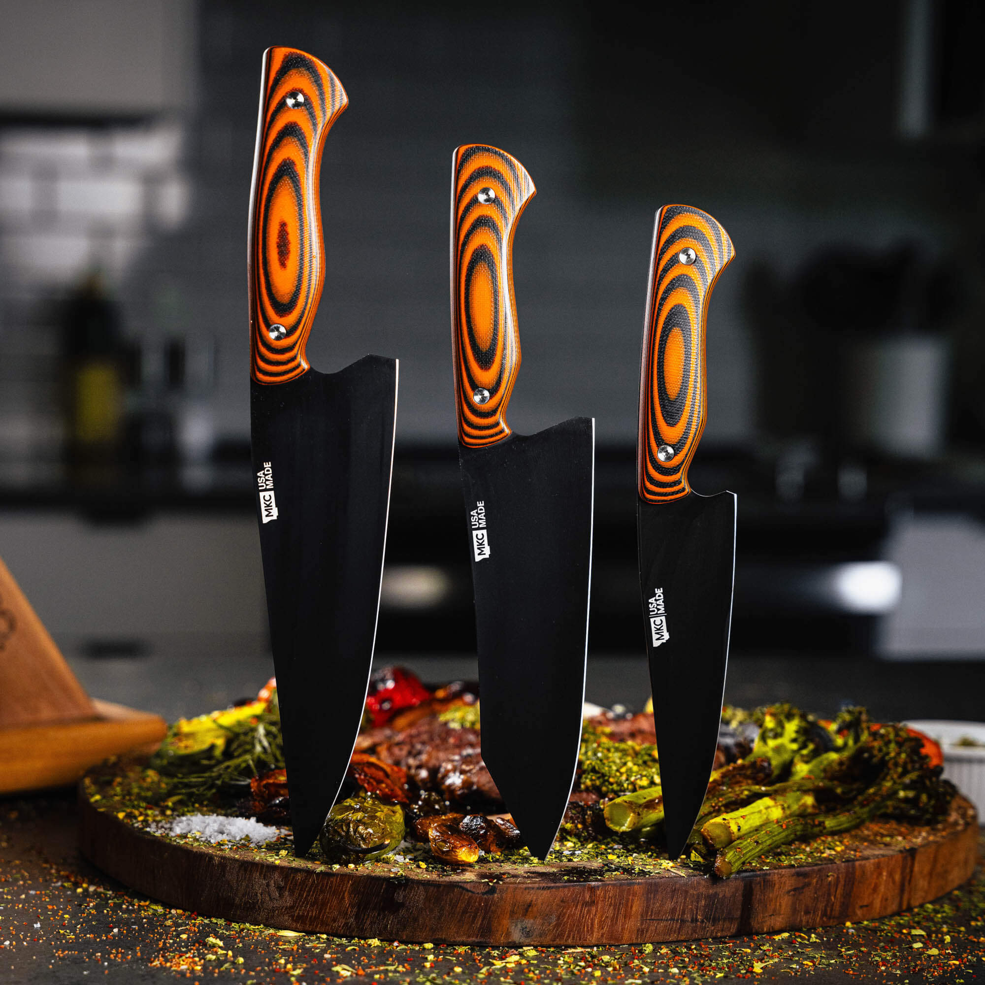 MKC Culinary Set featuring three knives with orange and black handles, displayed on a wooden cutting board with food.