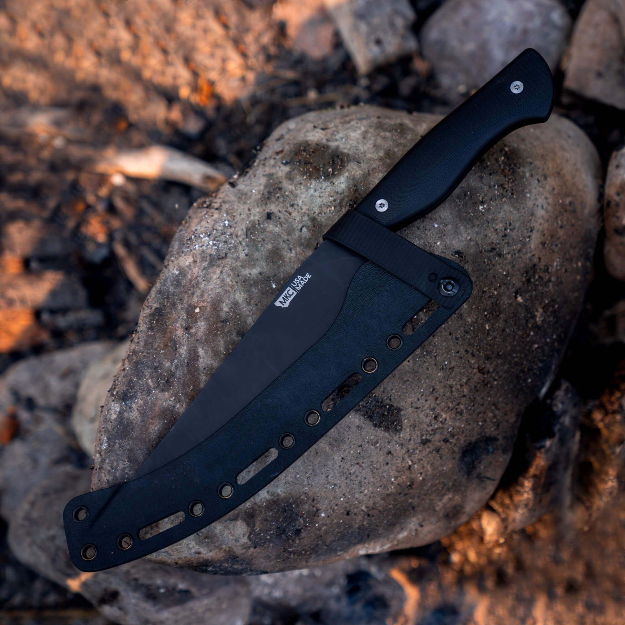 Alt text: "BIGHORN CHEF - BLACK tactical knife resting on a rugged rock, featuring a matte black finish and grippy handle, ideal for outdoor culinary use."