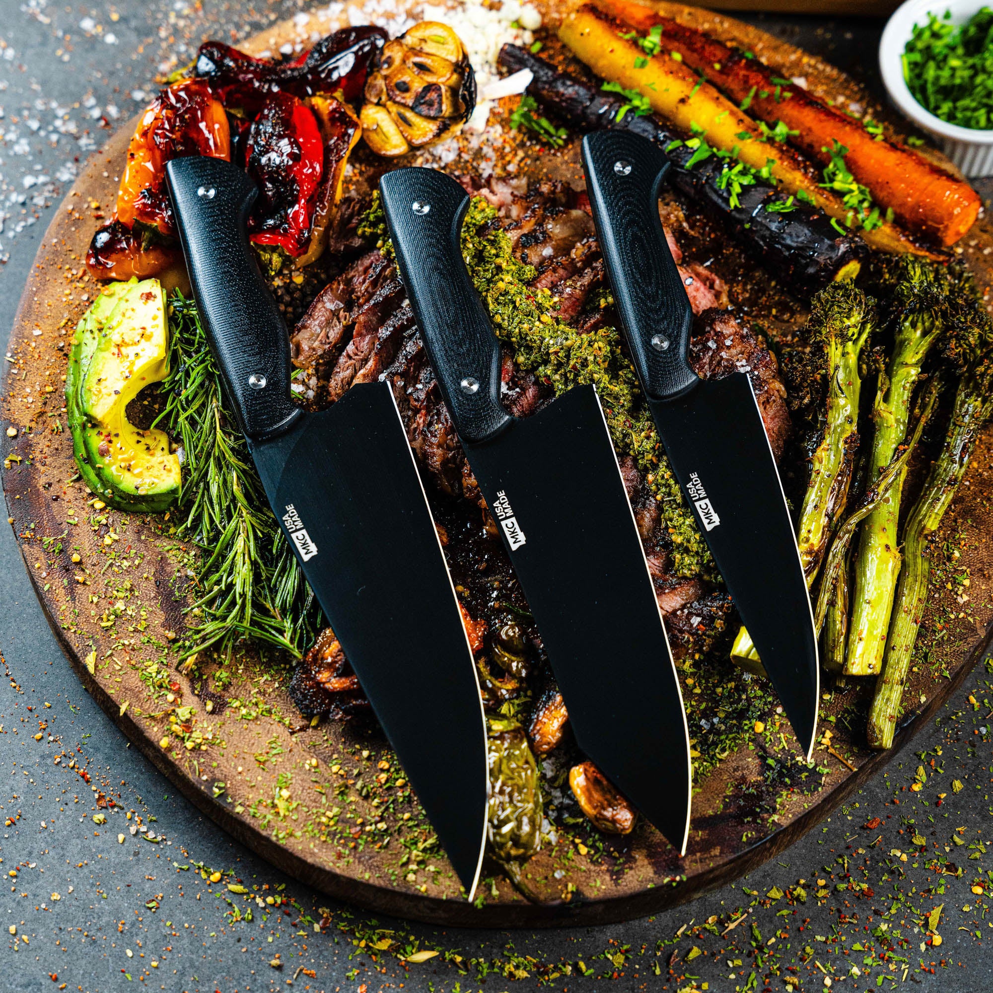 MKC Culinary Set in black displayed on a wooden platter with grilled meats and vegetables, showcasing three knives.