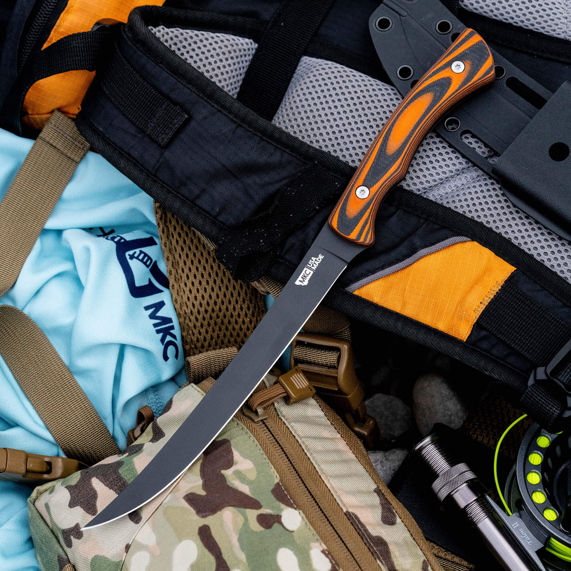 HUK Flathead Fillet knife with a black blade and orange handle, resting on outdoor gear and a tactical bag.