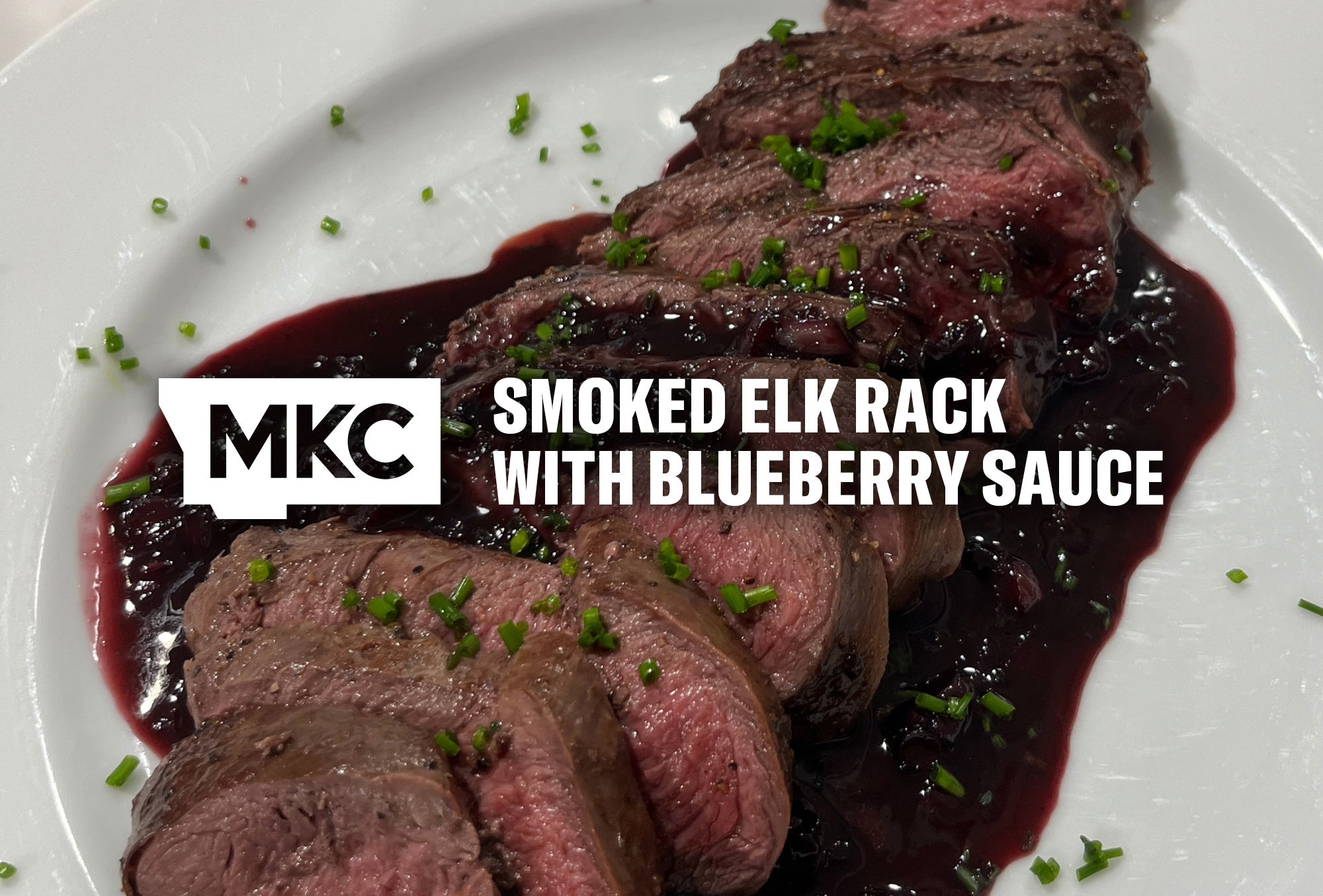 Smoked elk rack sliced and topped with blueberry sauce and herbs on a serving plate.