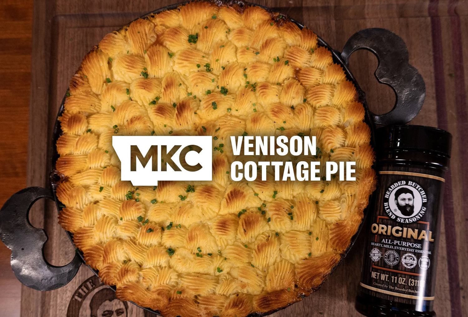 Golden venison cottage pie topped with browned mashed potatoes beside a Bearded Butcher seasoning jar.