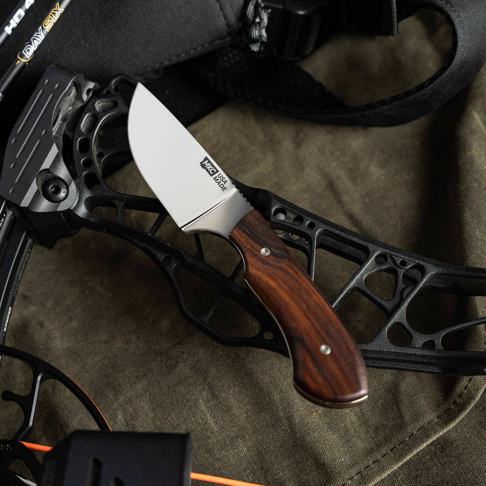 MKC Elk Knife with a sleek blade and wooden handle, resting on a black bow riser, showcasing its rugged design.