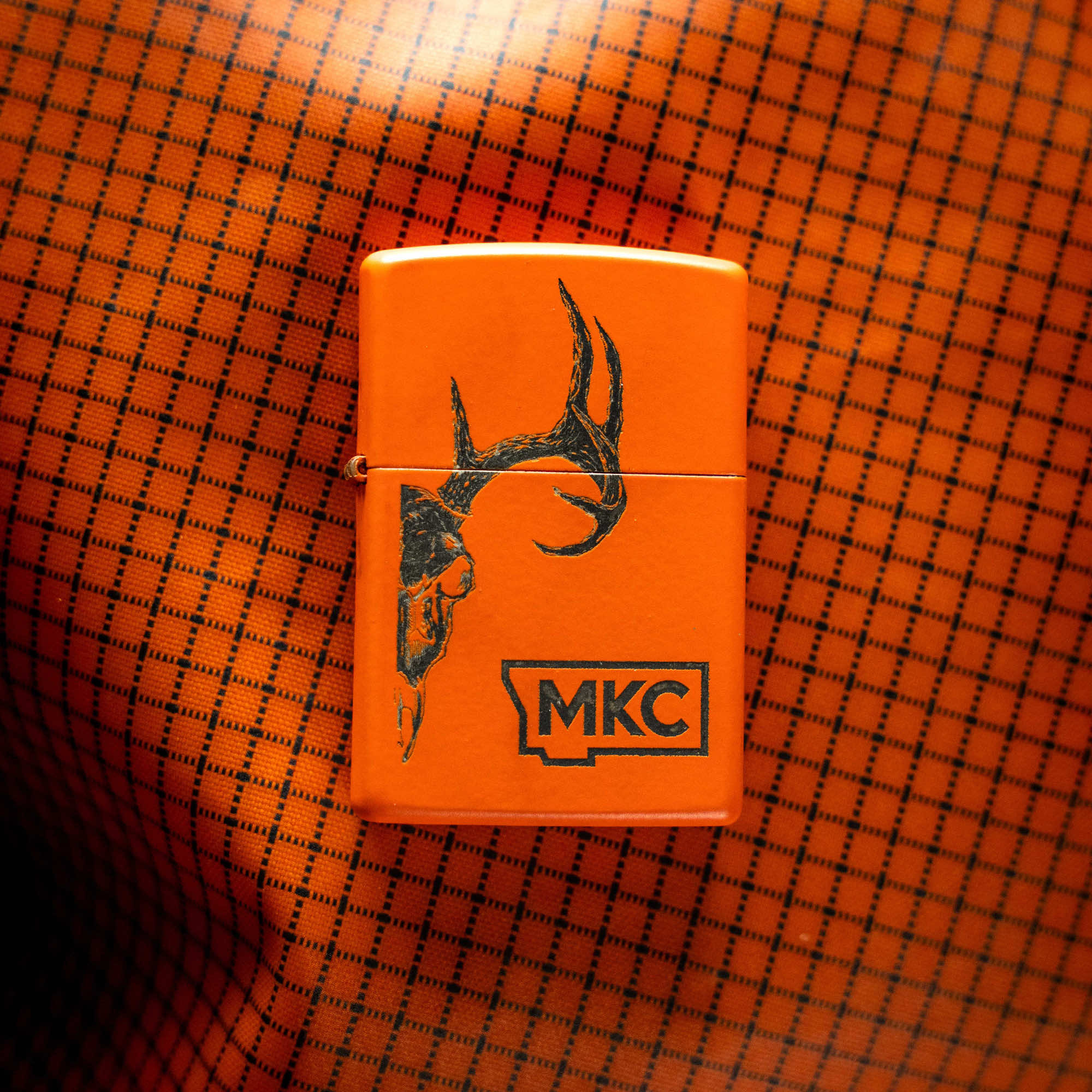 Limited edition blaze orange Zippo lighter with deer antler design, made in the USA, on an orange patterned background.