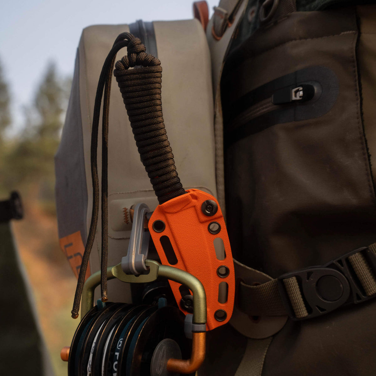 Blaze orange Cerakote MINI SPEEDGOAT 2.0 knife attached to a backpack with gear, showcasing its rugged design.