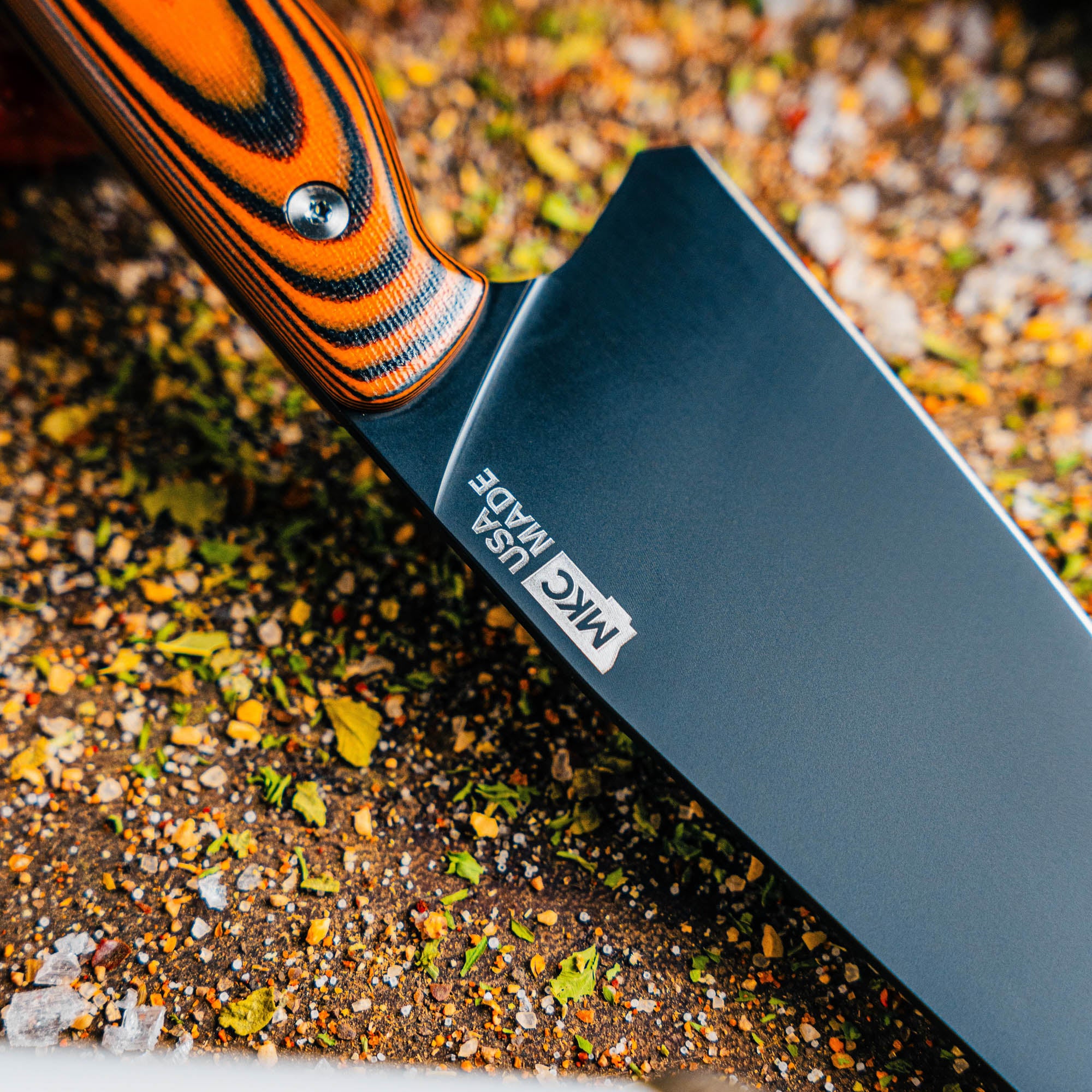 Meat Church chef knife with orange and black handle, featuring a sleek black blade, resting on a textured surface.