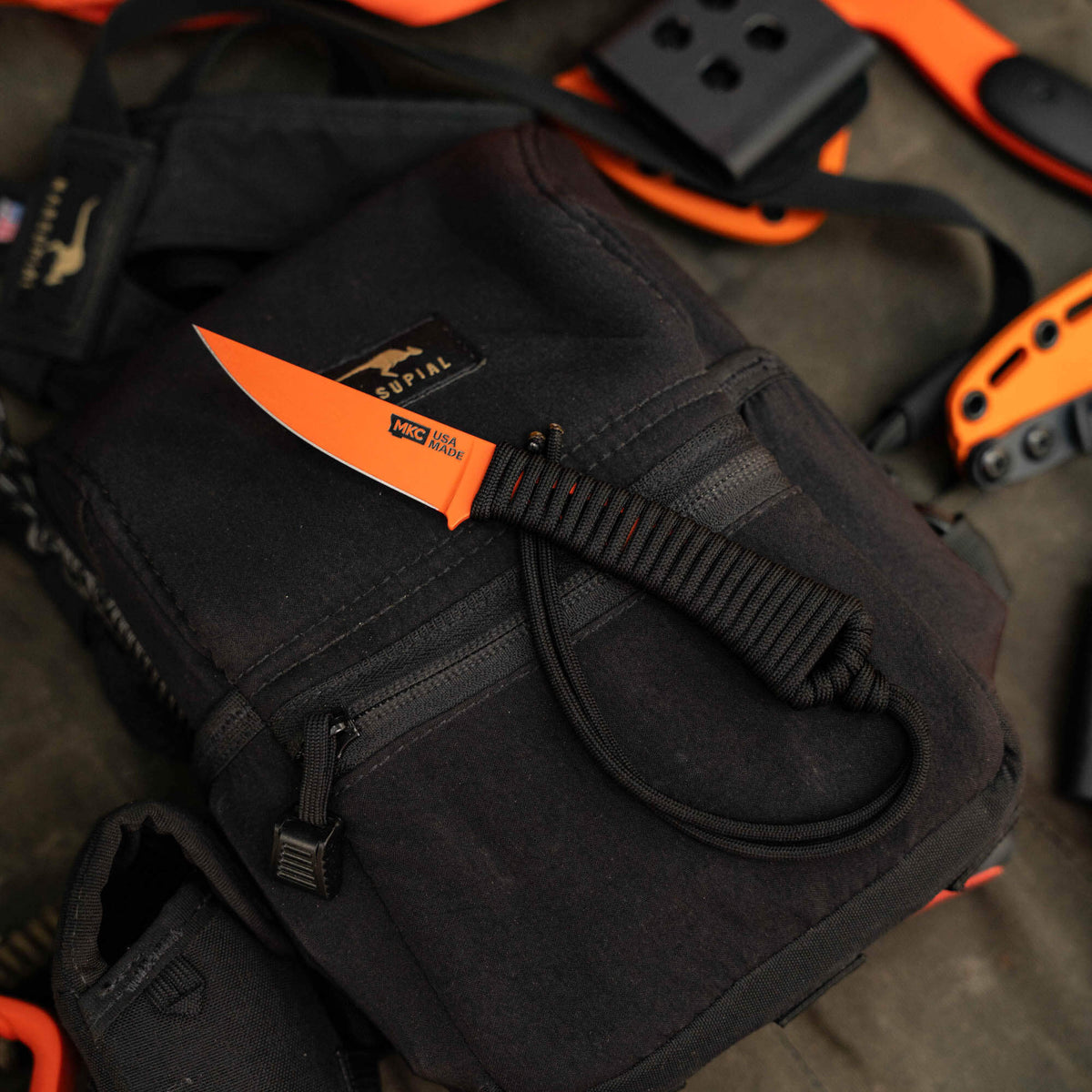 Mini Speedgoat 2.0 knife with blaze orange Cerakote finish on a black backpack, showcasing its compact design and functionality.