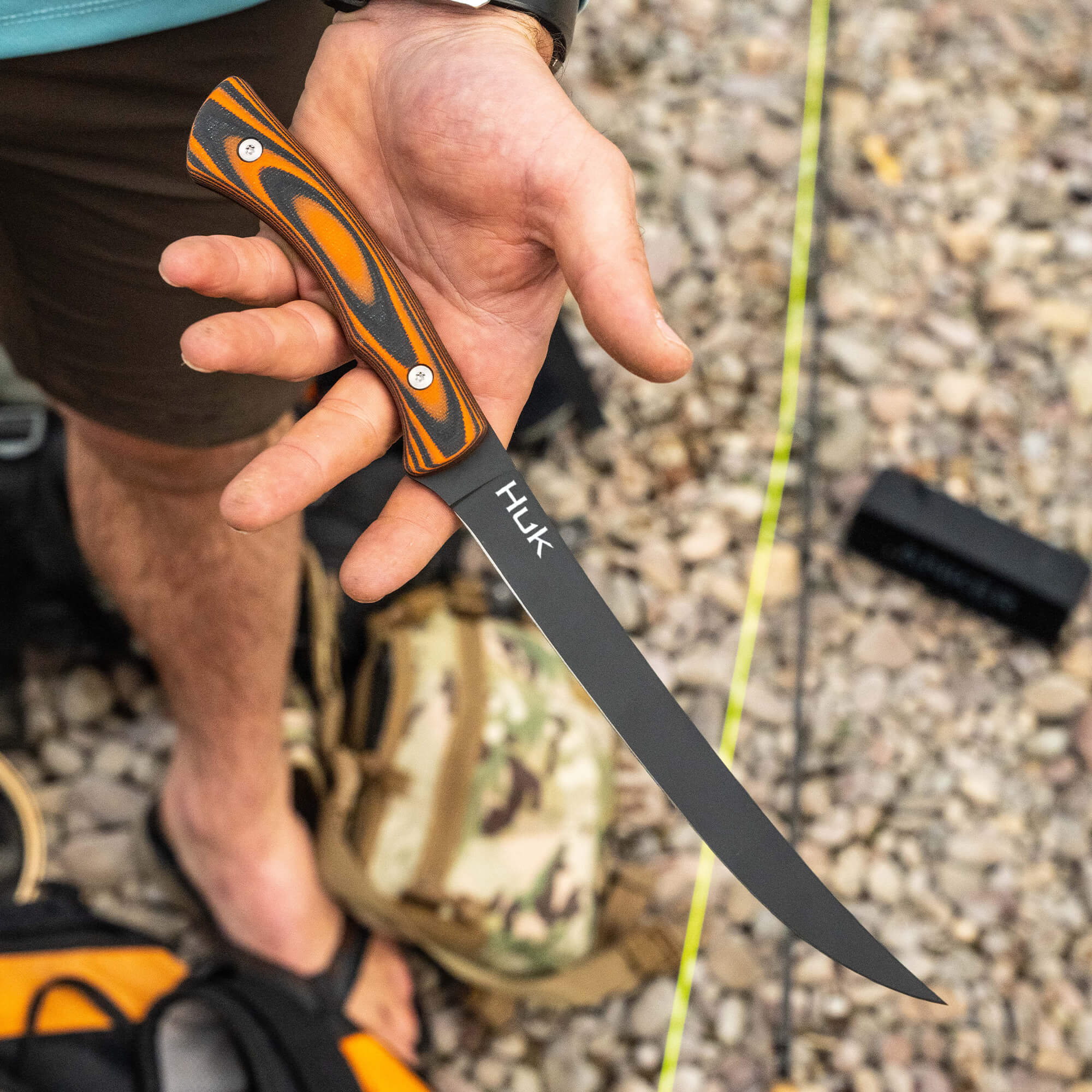 HUK Flathead Fillet knife held in a hand, featuring a curved blade and an orange and black handle, ideal for fishing.