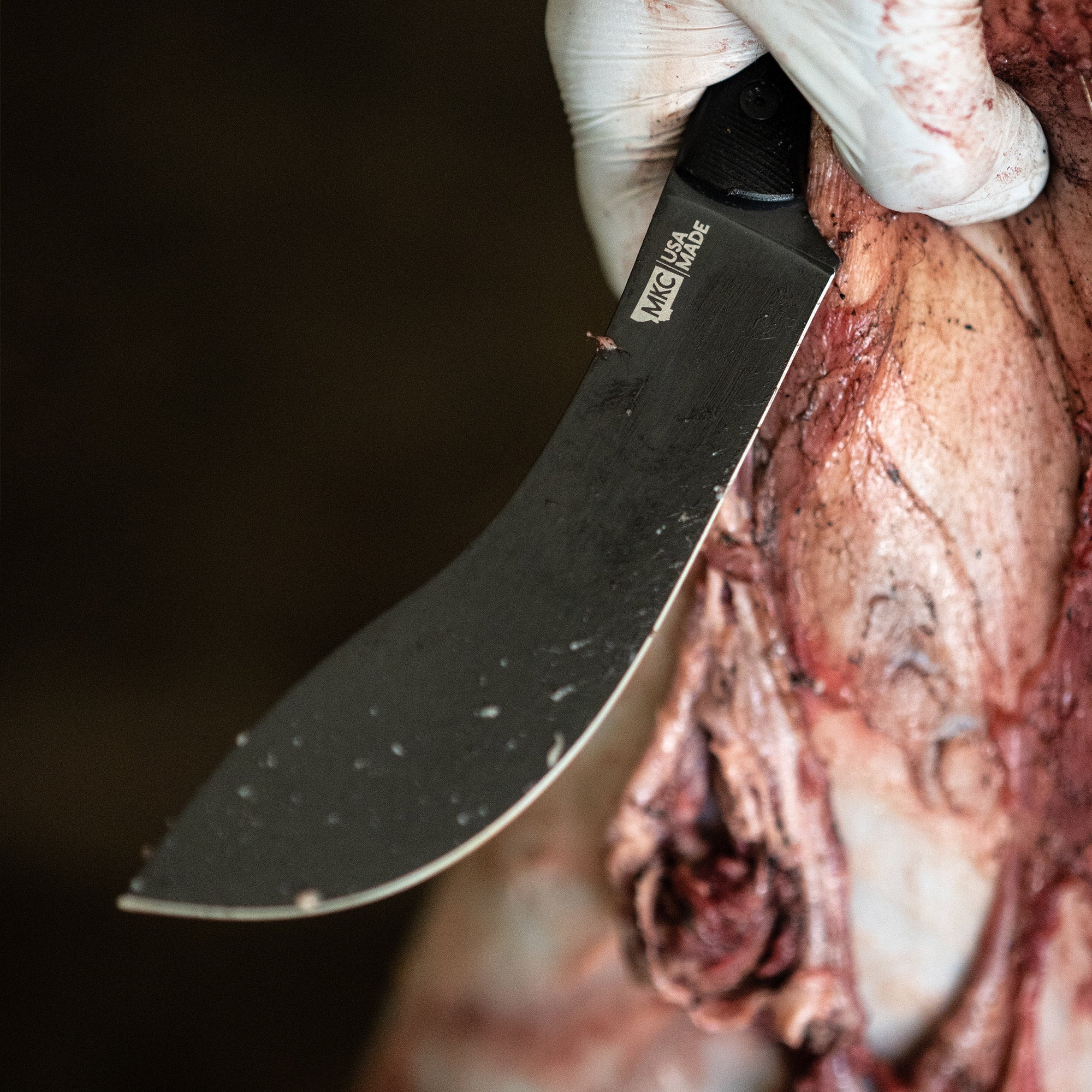 Close-up of a Beartooth Pro Skinning Blade in black, being used on animal carcass, highlighting the blade's curve and sharpness.
