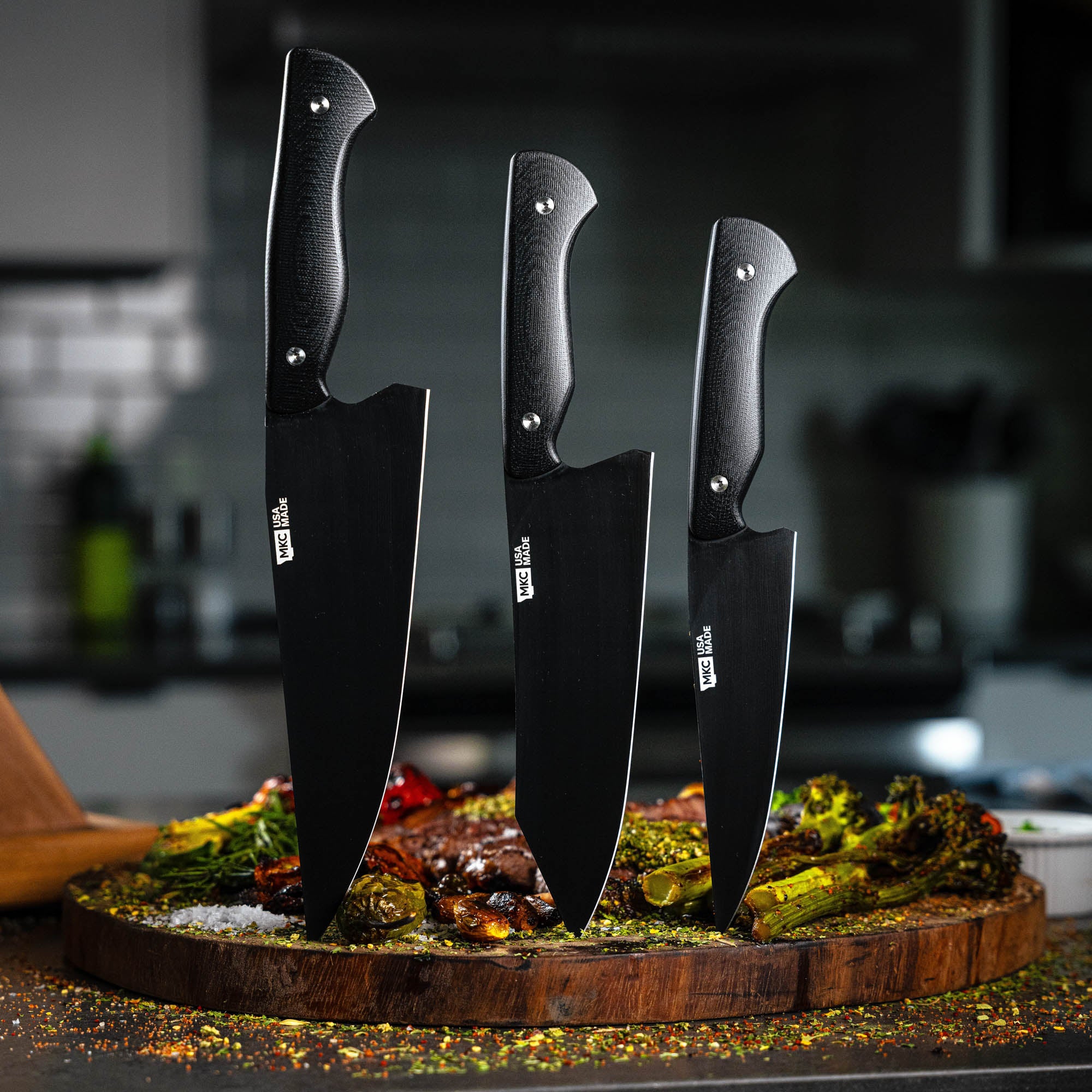 MKC Culinary Set in black featuring three knives on a wooden cutting board with vegetables and meat, showcasing quality craftsmanship.