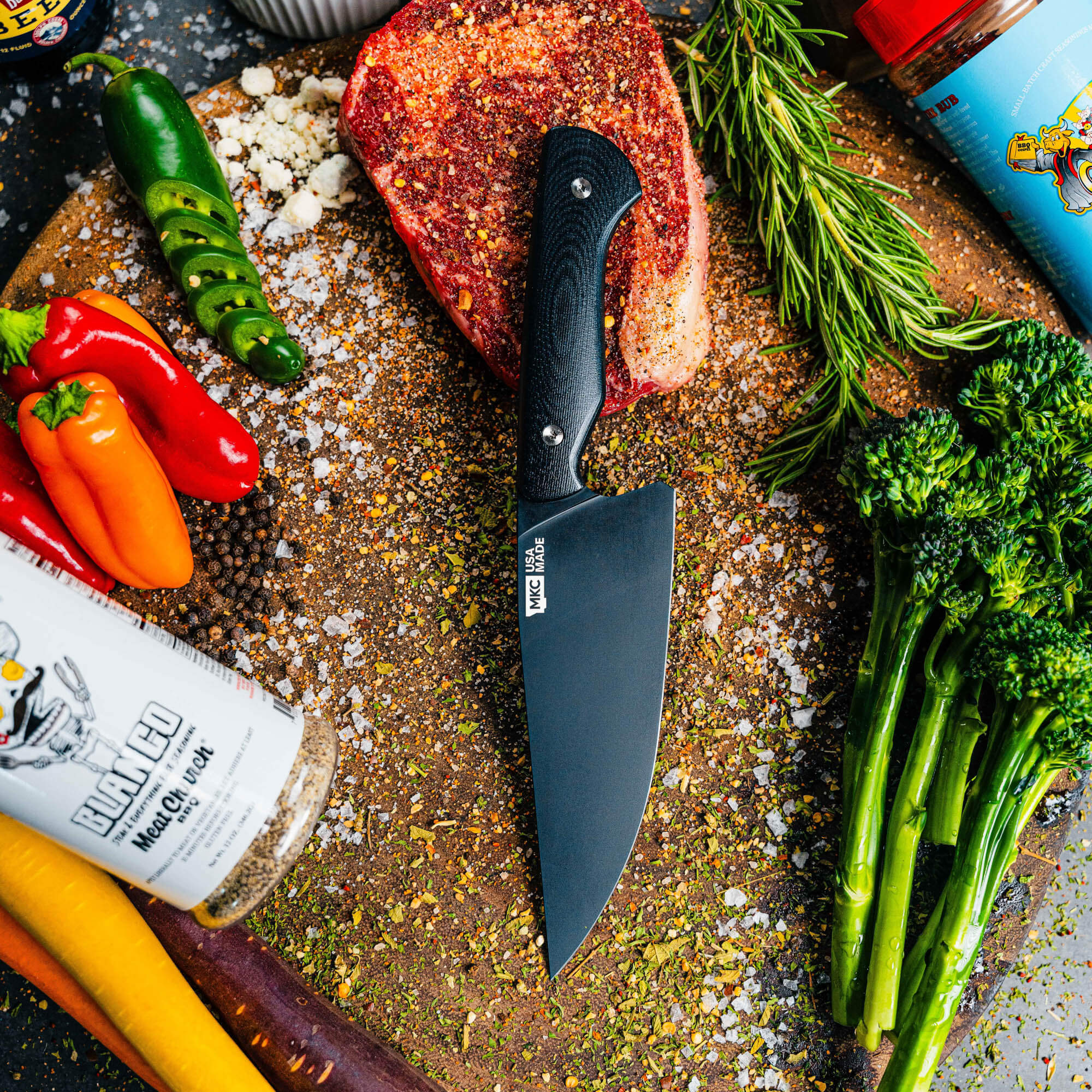 Black Meat Church chef knife displayed on a cutting board surrounded by fresh vegetables and spices, ideal for culinary tasks.