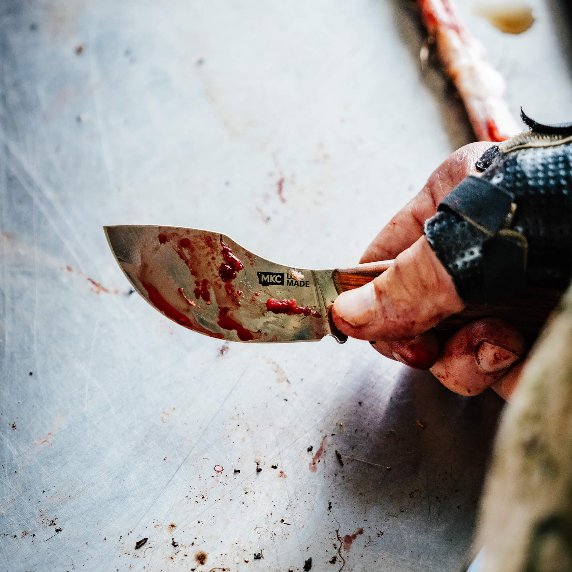 Close-up of a blood-stained Traditions Packout Skinner knife held by a hand, showcasing its rugged design and craftsmanship.