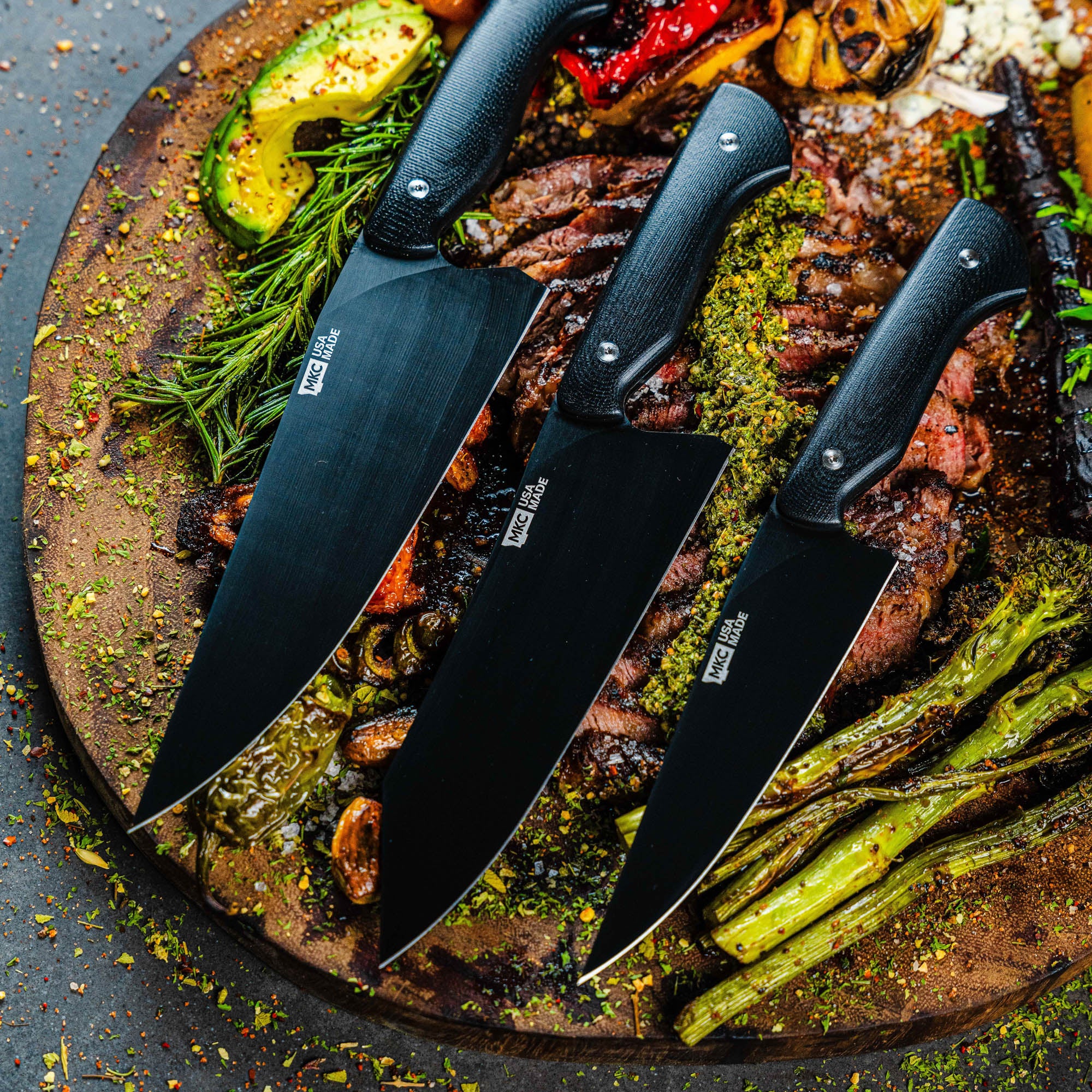 MKC Culinary Set in black featuring three high-quality knives displayed on a wooden board with grilled meats and vegetables.