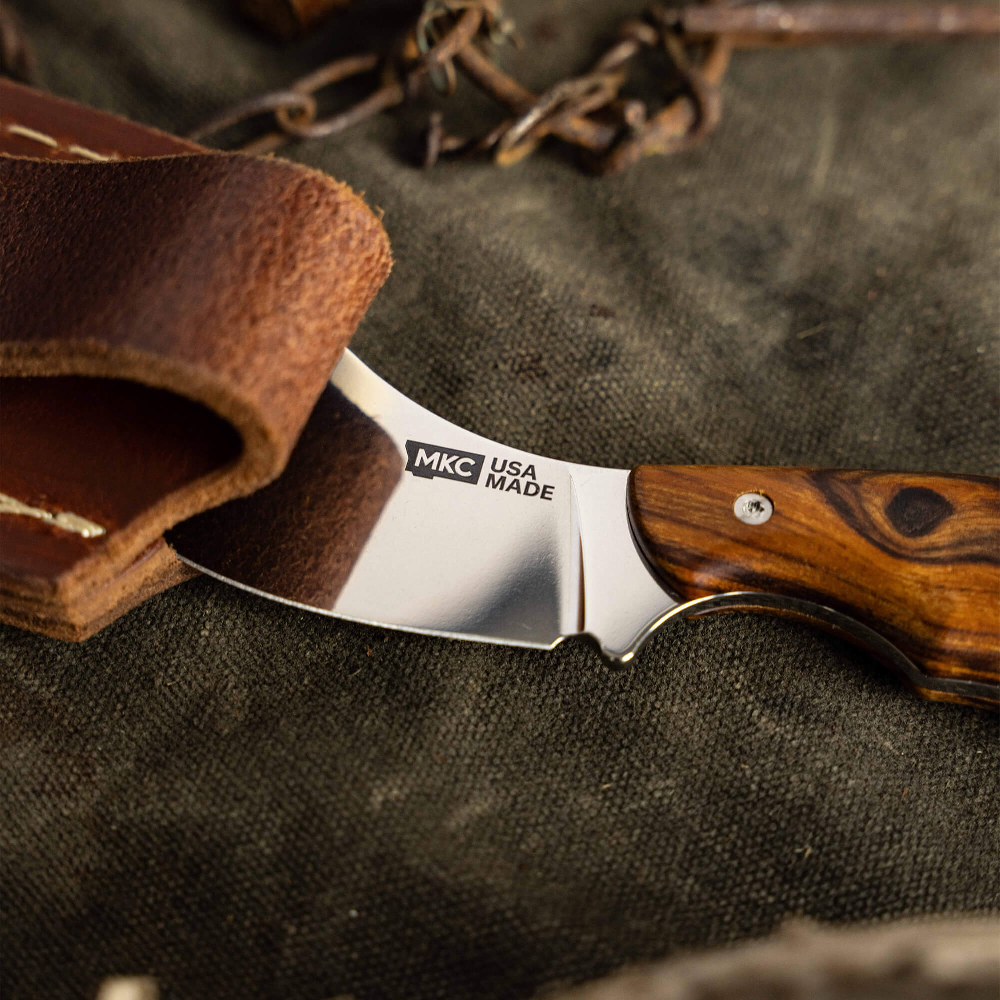 Montana Knife Company Keep Hammering Traditions Packout Skinner with a polished blade and wooden handle on leather background.