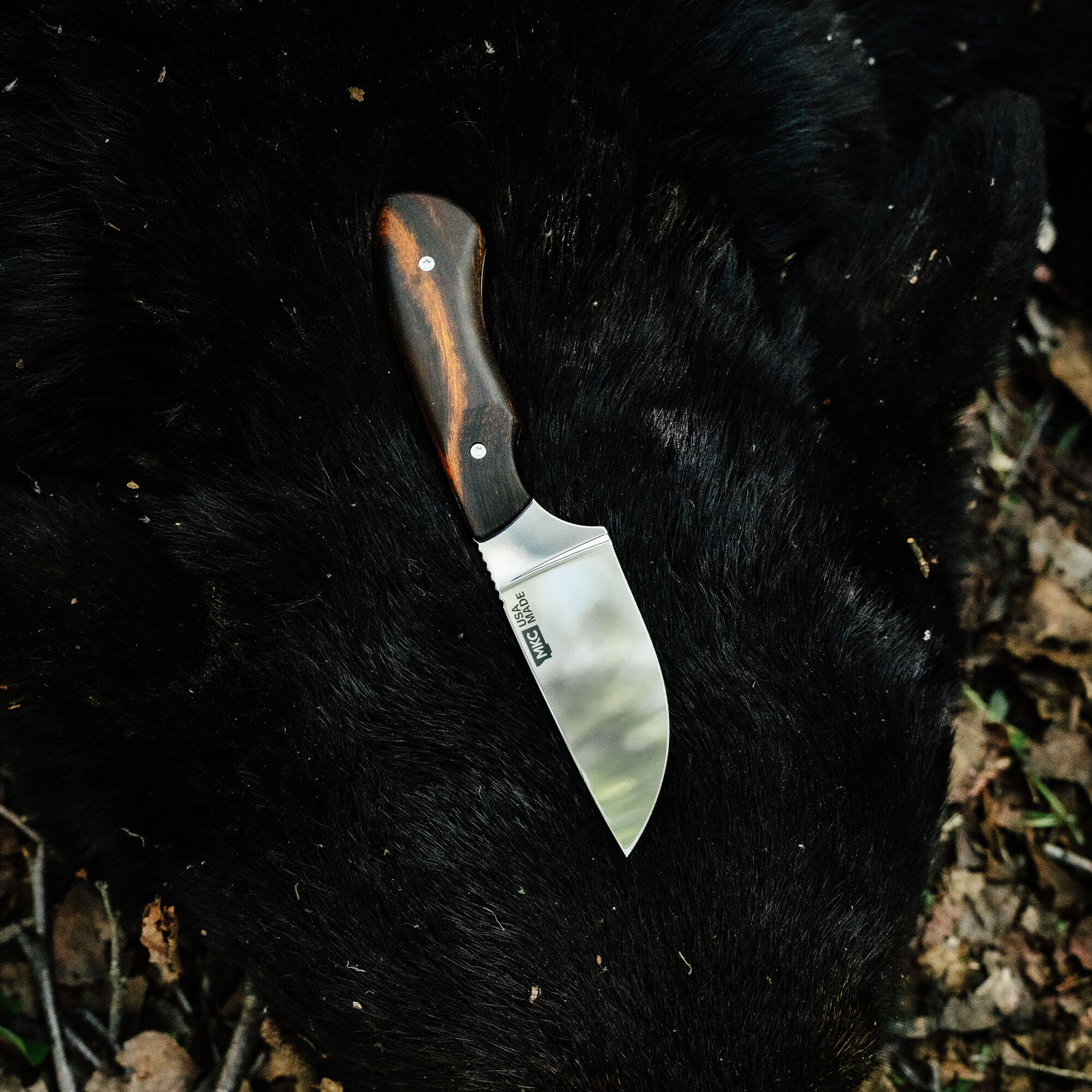 Elk knife with a curved stainless steel blade and wooden handle resting on a dark fur background, showcasing its craftsmanship.