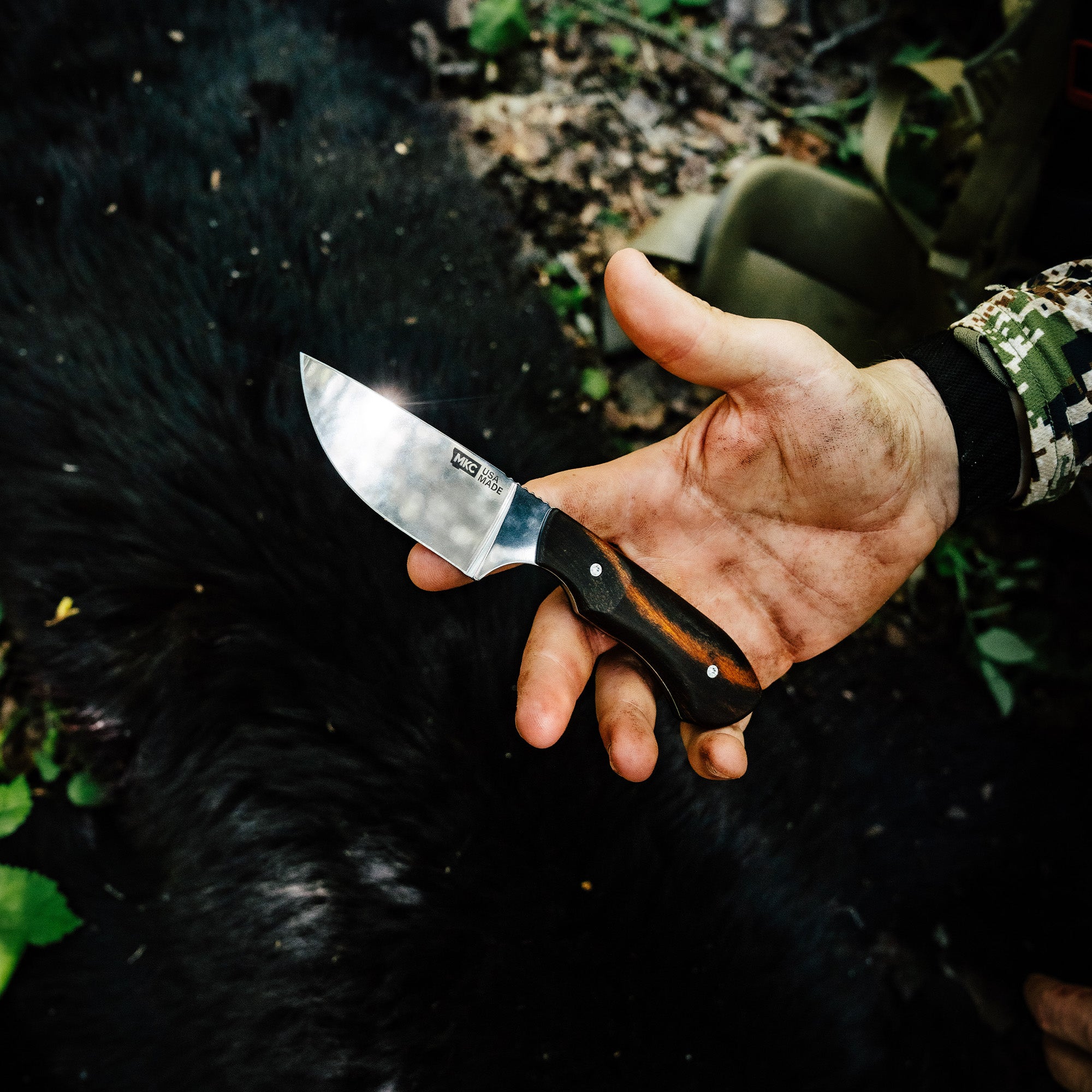 Hand holding the LIVE WILD Traditions MKC Elk Knife, showcasing its sleek blade and wooden handle against a natural background.